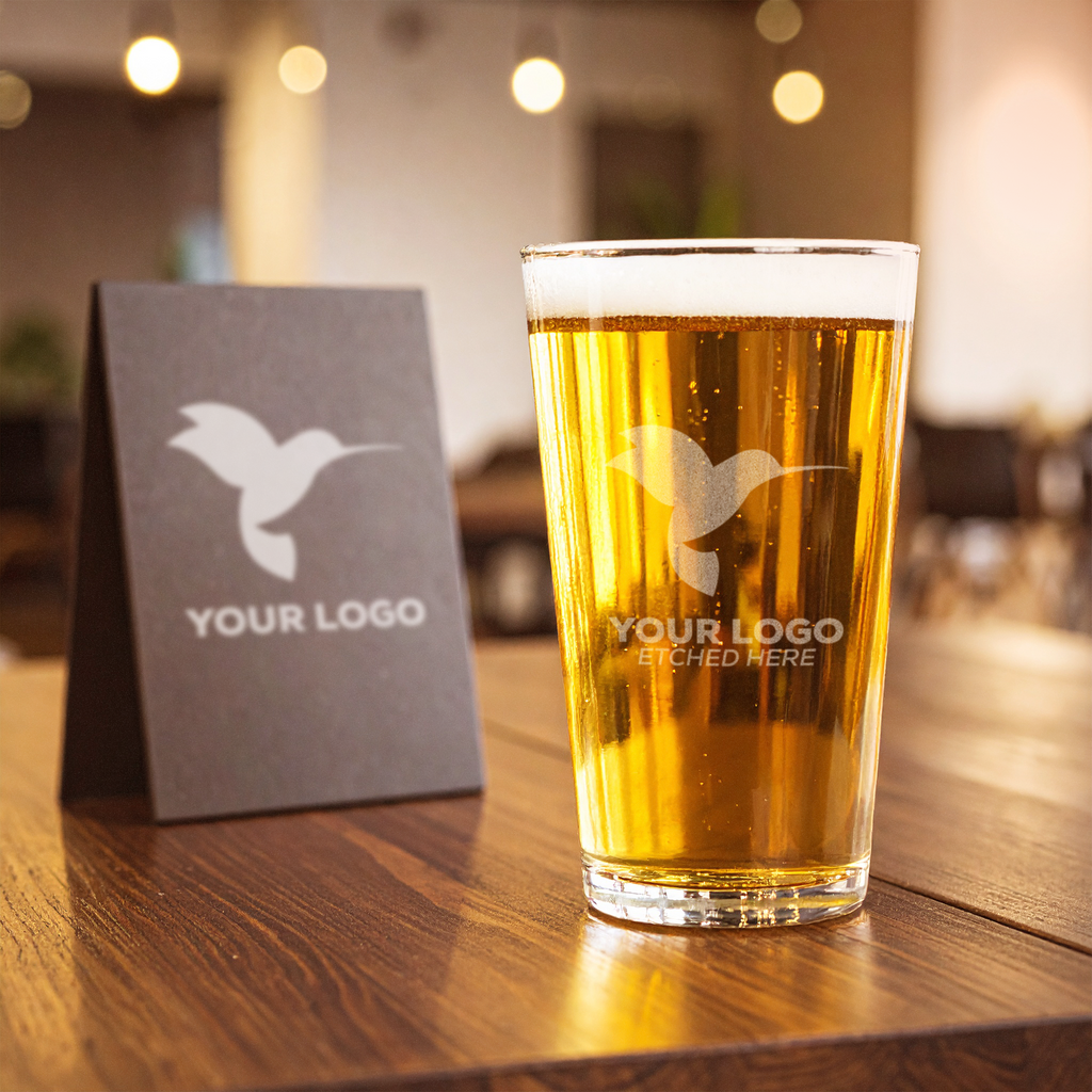 Personalized beer glass with etched logo displayed beside branded signage—perfect for trade show giveaways, corporate branding, or client gift sets.