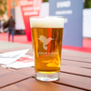 Custom beer pint glass with etched logo showcased at a corporate outdoor event—ideal for networking receptions, branded promos, and business expos.