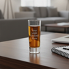Glass of beer with 'Your Logo Etched Here' text on a wooden table in a blurred living room setting.